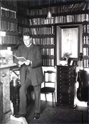 Glass negative of man in book-lined room.