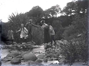 Glass negative of Baker family crossing a stream on stepping stones