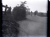 Glass negative of lane, with two figures and several gates.