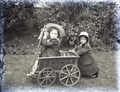 Glass negative of two Baker children with cart.