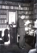 Glass negative of man in book-lined room.